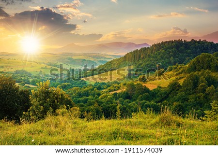 mountainous rural landscape at sunset. beautiful scenery with forests, hills and meadows in evening light. ridge with high peak in the distance. village in the distant valley Royalty-Free Stock Photo #1911574039