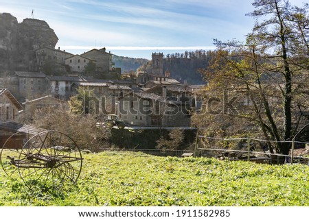 Amazing view of the ancient medieval village of Rupit from a field with old iron wheels trailer and a tractor.Traveling countryside concept background.