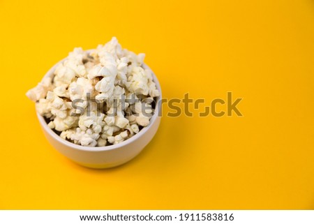 Bowl with popcorn on yellow background and space for text. Home cinema.