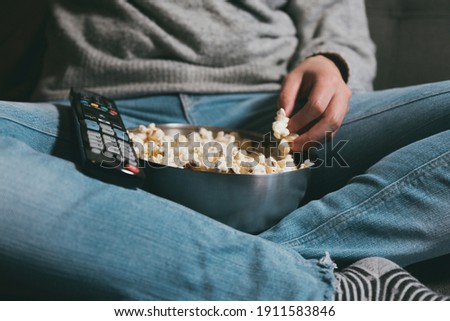 Close-up of a girl's body with a TV remote control and eating popcorn. Evening plan at home