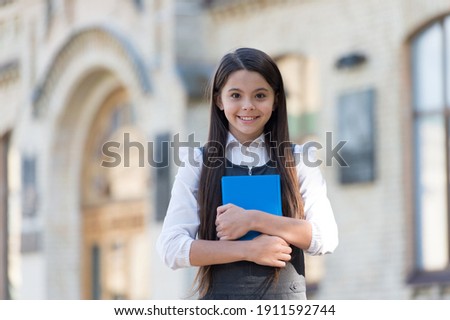 Happy small kid with school look wear uniform holding library book outdoors, knowledge. Royalty-Free Stock Photo #1911592744