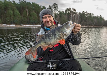 Happy fisherman hold big perch fish at boat with tackle. Success fishing at wild lake Royalty-Free Stock Photo #1911624394