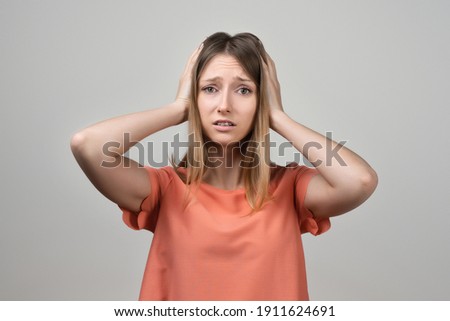 Portrait of concerned, worried and anxious blond girl, grab head and panicking, staring alarmed, feel scared and nervous, dont know what do. Studio shot, gray background