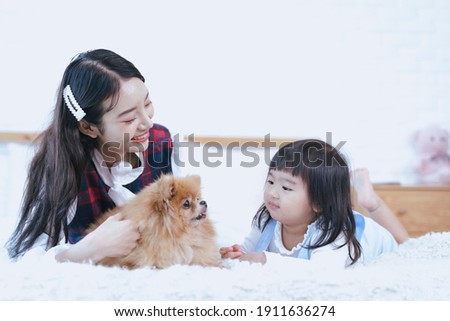 Two girls playing with a small dog in the bed. Pomeranian in bed with a girl. 