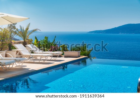 Summer vacation at poolside. Veranda decorated with deck chairs and umbrella with an ocean view Royalty-Free Stock Photo #1911639364