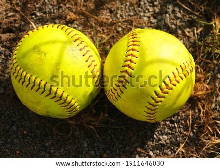 Two yellow softballs on the ground together with red lacing