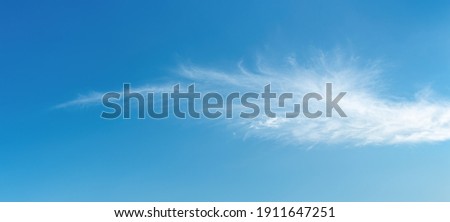 Angel wing shaped cloud against azure heaven. White cloud like a swan wing high in a blue sky. Translucent cirrus spindrift clouds high up. Purity and serenity concepts. Panoramic skyscape shot. Royalty-Free Stock Photo #1911647251