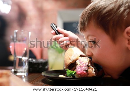 Portrait of child has burger in dark restaurant
