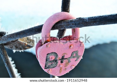 Iron wedding lock in pink color in the shape of a heart with an inscription:B+D. Over the winter river