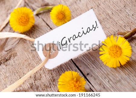 The Spanisch Word Gracias, which means Thanks, on a white Banner with Yellow Flowers