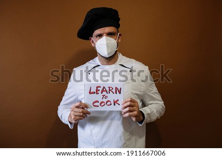 Chef man holding a sign that says learn and cook, He wears a mask on his face
