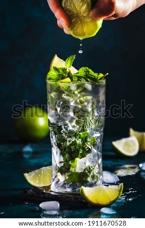 Mojito cocktail, alcohol long drink making. Mint, lime, ice, white rum on blue background. Bartender squeezes lime juice into glass Royalty-Free Stock Photo #1911670528