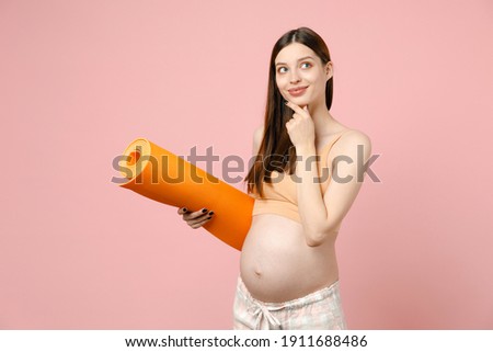 Young strong sporty fitness pregnant woman keeping hands on big belly stomach tummy with baby holding yoga mat isolated on pastel pink background studio. Maternity family pregnancy expectation concept