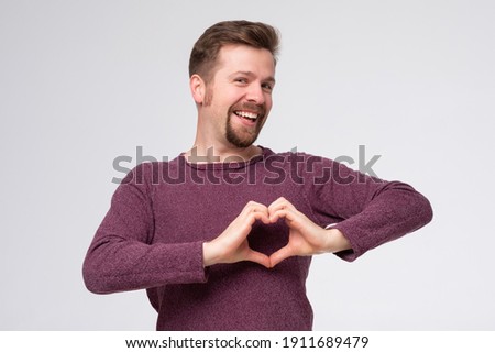 Young man with beard smiling in love doing heart symbol shape with hands. Romantic concept.