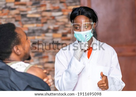medical personnel wearing a face mask and shield and holding a syringe gives a patient a thumbs up
