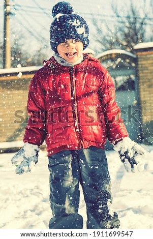 Excited Child playing with snow on white snow background. smiling boy catching snowflakes. Funny little boy in blue winter clothes walks during a snowfall. Outdoors winter activities for kids. toned.