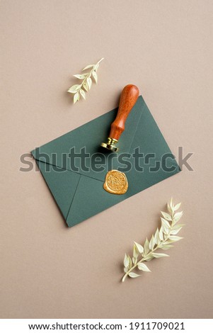 Green paper envelope with wax seal stamp and dried leaves on pastel beige background. Flat lay, top view. Romantic letter concept.