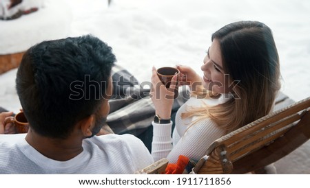 Back view. Happy young couple drinking hot chocolate while sitting on the bench outdoors on Valentines day. High quality photo
