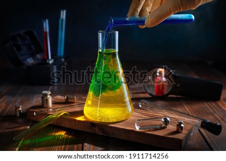 scientist pours blue liquid into yellow in a chemical flask. color change. science, experiments Royalty-Free Stock Photo #1911714256