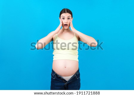 Picture of shocked or surprised pregnant lady standing over colored background. Looking at camera.