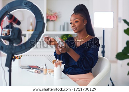 happy young african american woman streaming a beauty vlog from home, online content creator applying a perfume fragrance