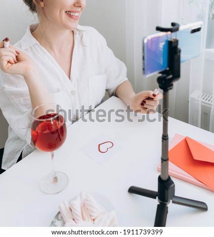 A woman who has a video call on her smartphone draws a greeting card with a heart. Remote acquaintance or declaration of love during quarantine. Virtual Valentine's Day.close-up