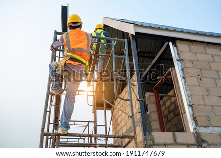 Construction worker wearing safety harness and safety line working on scaffolding at new house under construction. Royalty-Free Stock Photo #1911747679