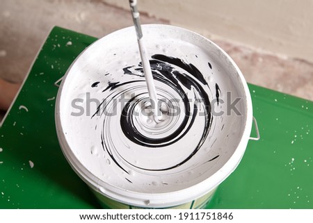 House painter mixes two paints using mixer for bucket with paddle mixing tool. Royalty-Free Stock Photo #1911751846
