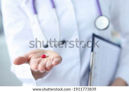 Red-white pill is on the doctor's hand. Medicines handbook concept