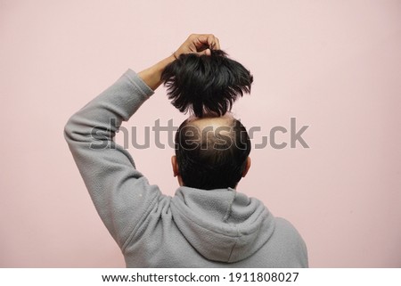 A closeup of a half-bald male removing his wig while wearing a hoodie with a pink background Royalty-Free Stock Photo #1911808027