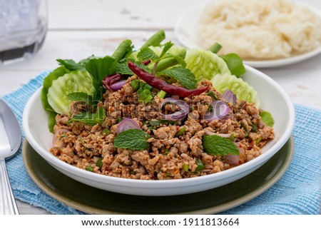Thai spicy minced pork salad or laab moo in Isan Thai food style, served on the white plate together with sticky rice. It is the tangy hot dish popularly served in Isan Thai food restaurants.  Royalty-Free Stock Photo #1911813664