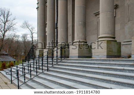Four large round concrete columns at the top of marble steps with black iron rails to a legal building. The government building has a tall red door.  The view is from the lower corner of the steps.