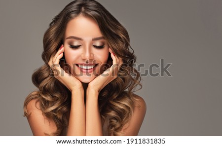 Beauty brunette girl with long shiny curly hair . Beautiful  smiling woman model  wavy hairstyle . Cosmetology, cosmetics and make-up. Royalty-Free Stock Photo #1911831835