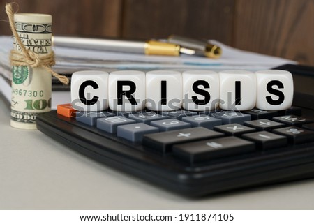 Business and finance concept. There are cubes on the calculator that say - CRISIS. Nearby out of focus - dollars, notebook and pen
