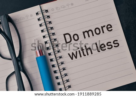Top view of eyeglasses, pen and notebook written with text DO MORE WITH LESS. 