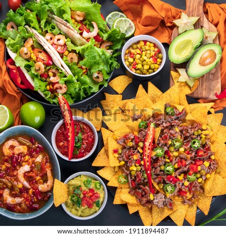Delicious hispanic mexican meal board with nachos, tacos, guacamole, shrimps, avocado and starfruit. Hot and spicy. Top view