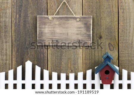 Blank wood sign over white picket fence with birdhouse