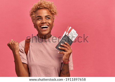 Photo of pleased dark skinned lovely young woman clenches fist wears lilac tshirt has overjoyed expression opens mouth, isolated over pink background with empty space for your text. Travel concept