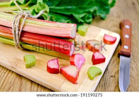 Bundle of stalks, pieces rhubarb, a sheet, a knife on a wooden boards background Royalty-Free Stock Photo #191190275