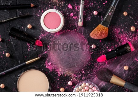 Makeup products and tools, forming a frame for copy space, overhead flat lay shot on a dark background
