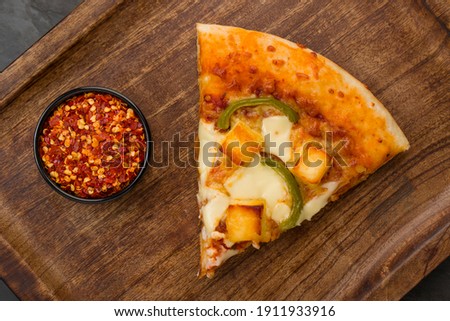 Pizza_Paneer Makhani , home made delicious  pizza  made using green bell pepper ,paneer and mozzarella cheese as topping on thin pastry crust piece  placed on a wooden board with grey background