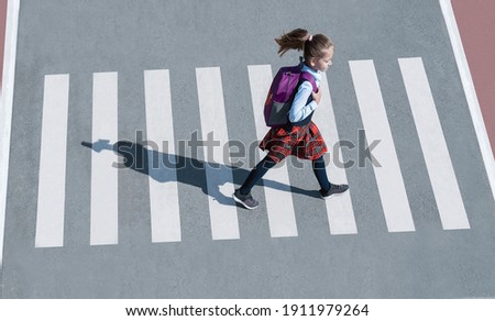 Schoolgirl crossing road on way to school. Zebra traffic walk way in the city. Concept pedestrians passing a crosswalk.  Stylish young teen girl walking with backpack. Active child. Top view Royalty-Free Stock Photo #1911979264