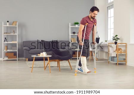 Successful rehabilitation and recovery of people after physical injury such as bone fracture in car or home accident: Young man with broken leg trying to walk with crutches and making good progress Royalty-Free Stock Photo #1911989704