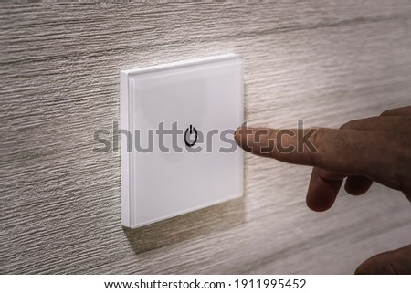 A close-up finger turns on the light on the touch switch. A white modern light switch on a white wall. modern design. turn-on turn-off Royalty-Free Stock Photo #1911995452