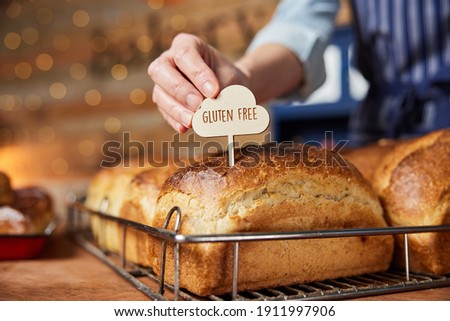 Sales Assistant In Bakery Putting Gluten Free Label Into Freshly Baked Baked Sourdough Loaves Of Bread Royalty-Free Stock Photo #1911997906
