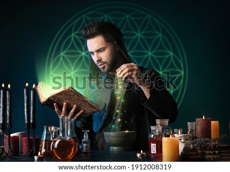Male alchemist making potion on dark background Royalty-Free Stock Photo #1912008319