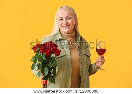 Mature woman with glass of wine and flowers on color background. Valentine's Day celebration