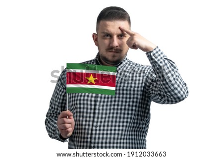 White guy holding a flag of Suriname and a finger touches the temple on the head isolated on a white background.