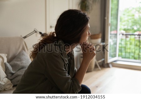 Pensive young Caucasian woman sit on sofa at home look in distance think ponder of family problem solution. Unhappy thoughtful millennial female troubled lost in thoughts, consider breakup or divorce. Royalty-Free Stock Photo #1912034155