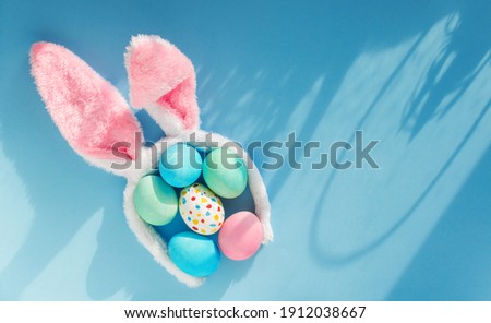happy easter creative bunny ears headband and colored eggs natural sun light effect flat lay on blue background